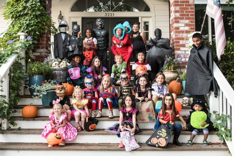 24 kids in Halloween costumes sit on a front porch