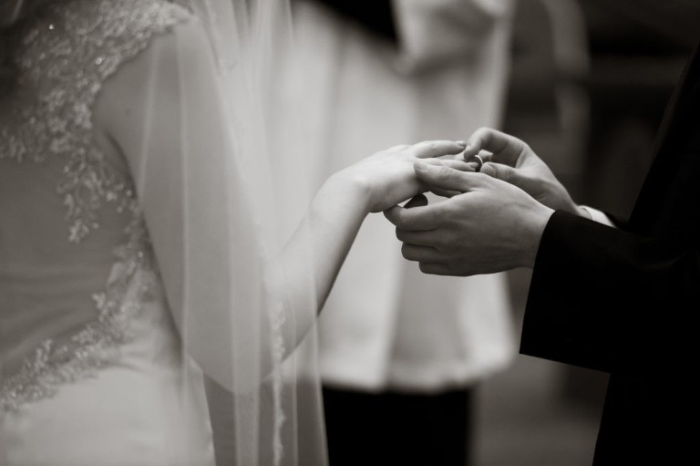 A groom is saying his vows as he places a wedding band on the bride's finger